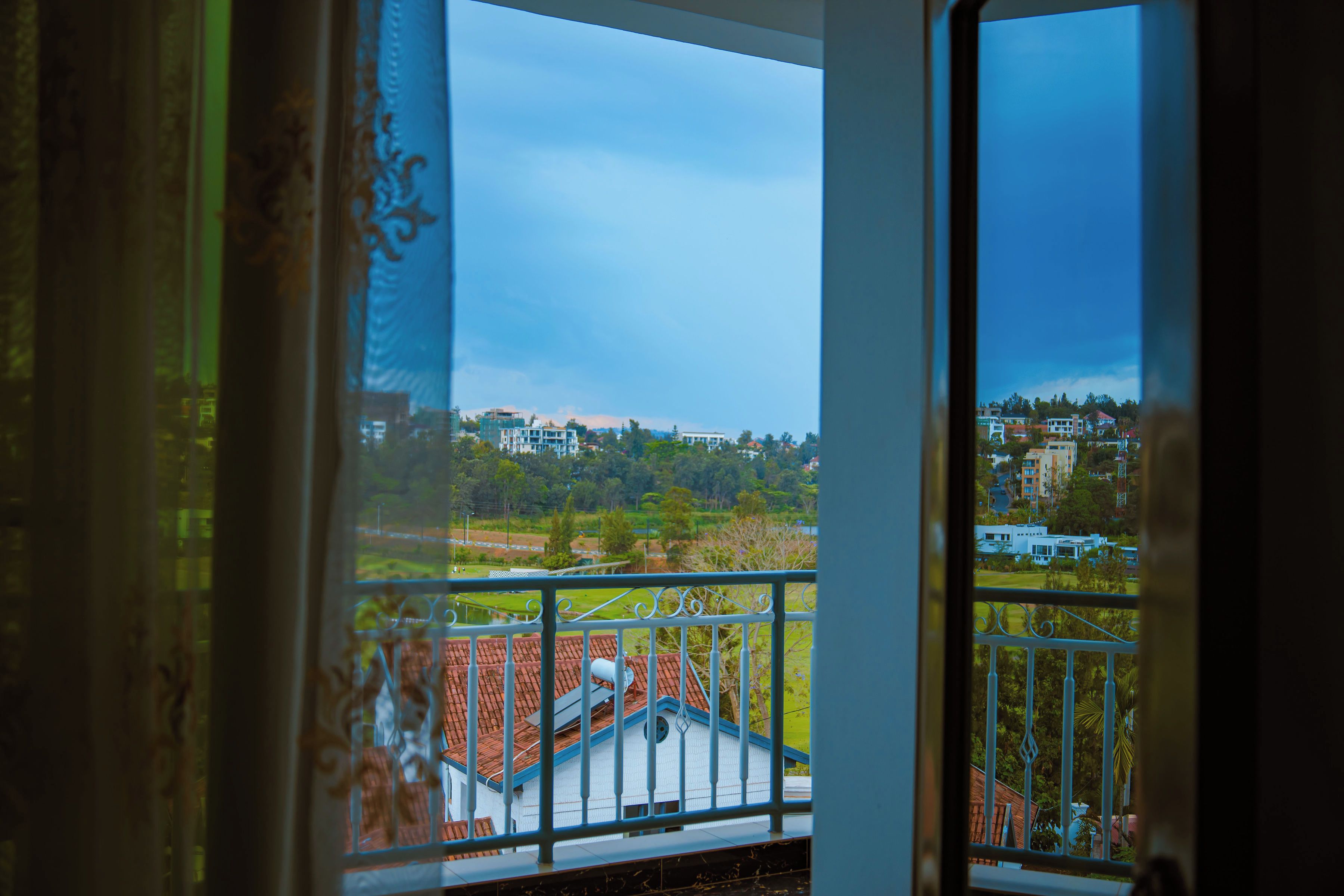 Une vue depuis un balcon doté d’une rambarde en métal, donnant sur un quartier résidentiel avec des maisons et de la verdure.