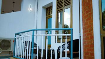 A balcony with a white railing, a window with blinds, and a view of the sky.