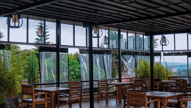 An indoor dining area with wooden tables and chairs, large windows, and hanging lanterns. - ROYAL CROWN HOTEL  (Kigali)