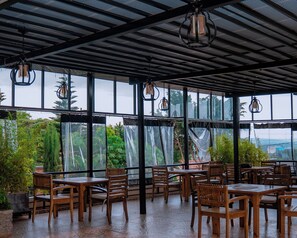 An indoor dining area with wooden tables and chairs, large windows, and hanging lanterns. - ROYAL CROWN HOTEL  (Kigali)