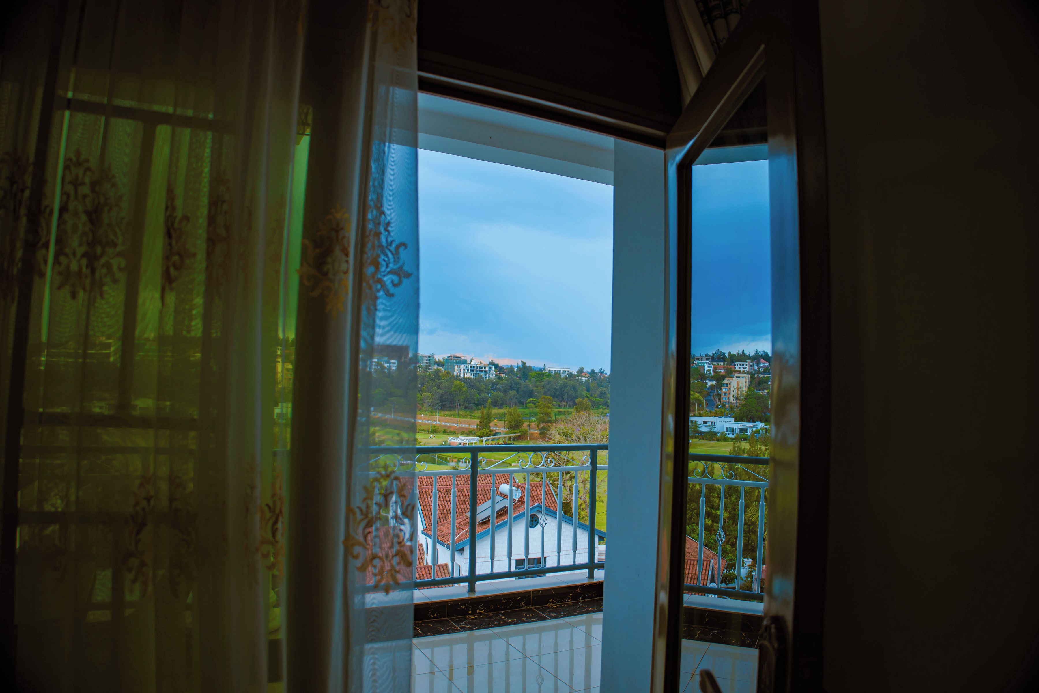 A view from a balcony with a metal railing, overlooking a residential area with houses and greenery.