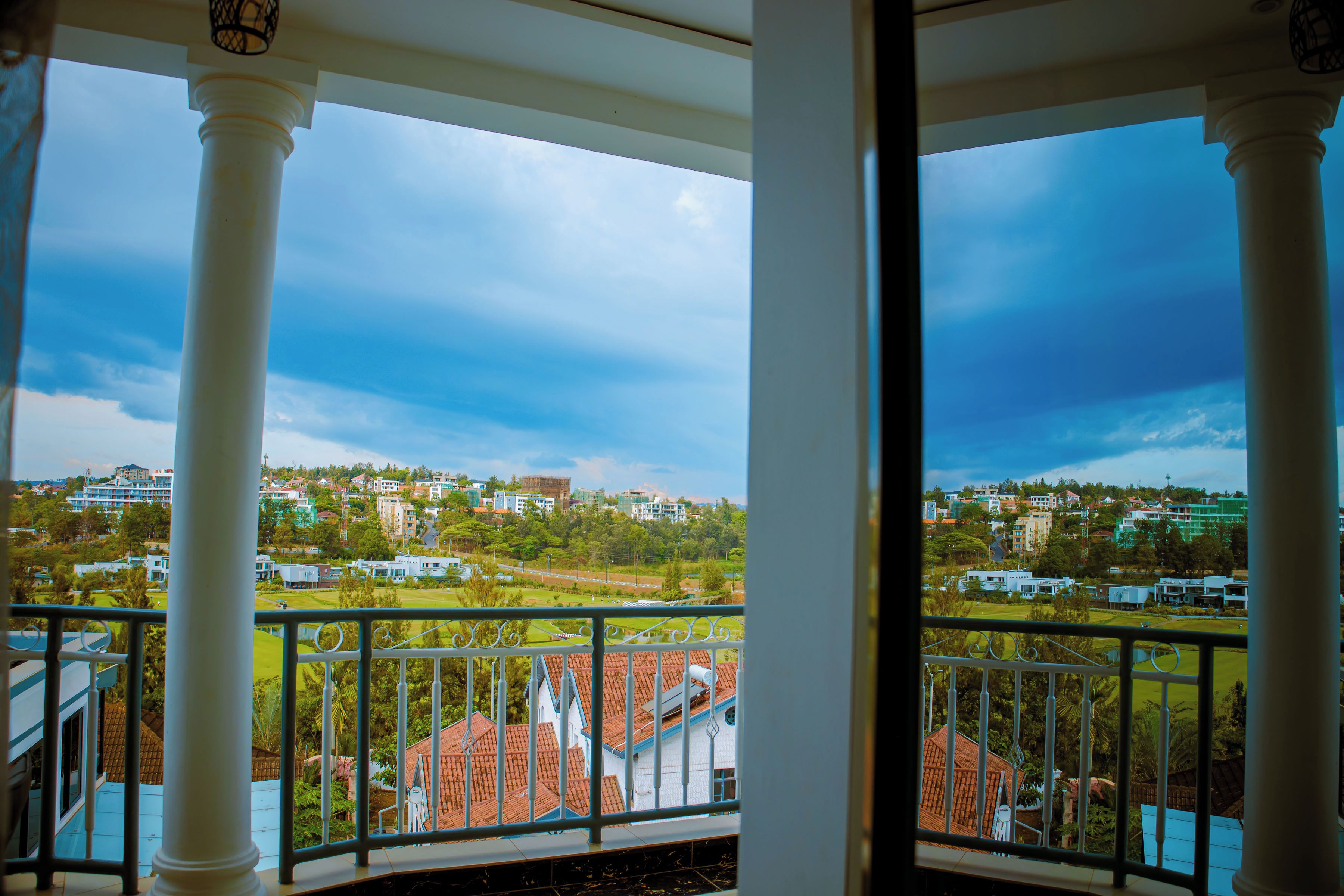 A balcony with white columns and a view of a residential area with houses and greenery.