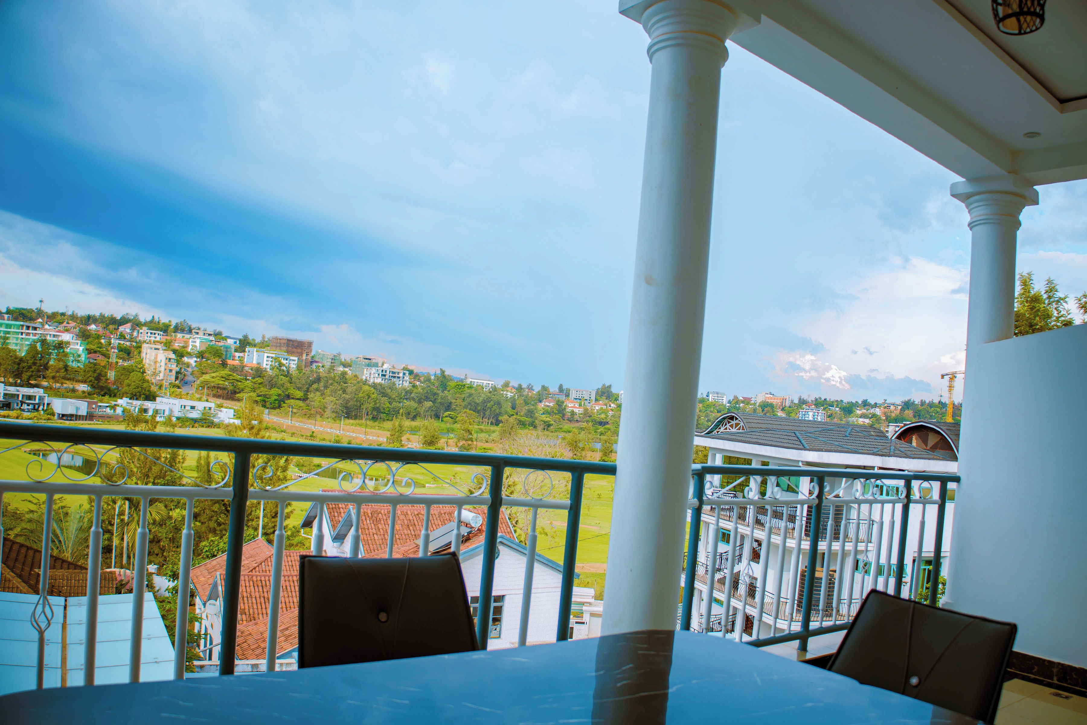 A balcony with a view of a residential area, a table, and chairs.