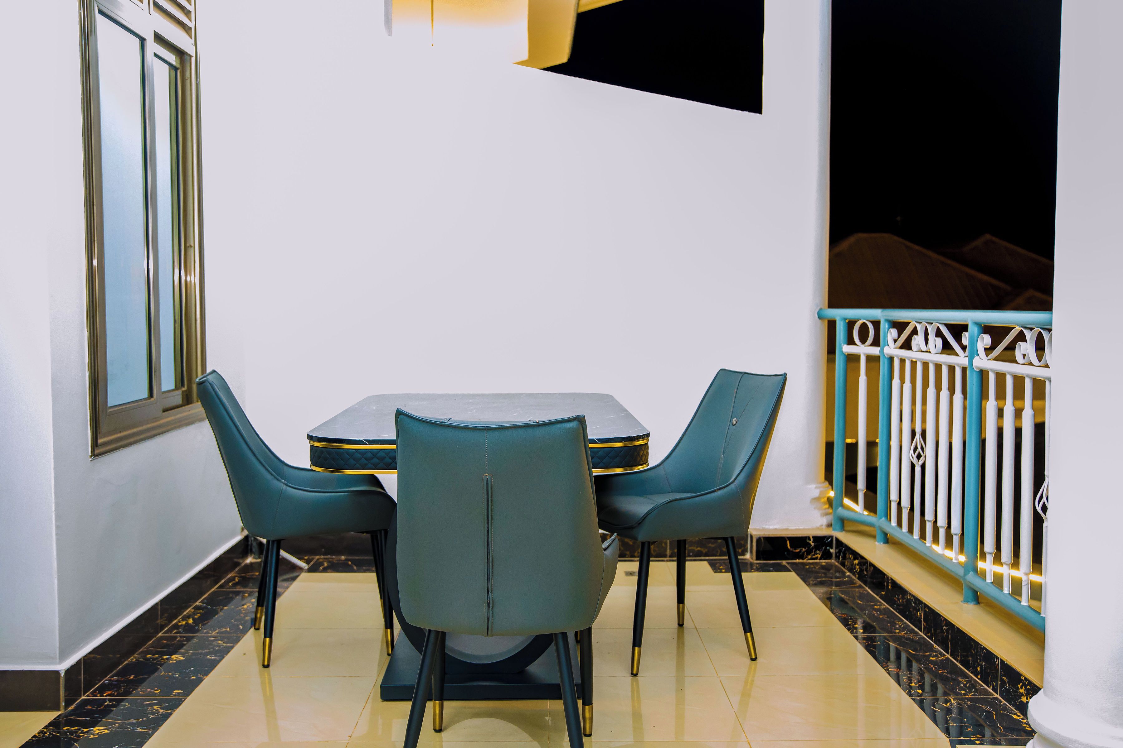 A dining area with a table and chairs, a TV mounted on the wall, and a balcony with a railing.