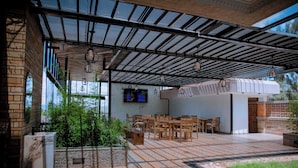 An outdoor patio with tiled flooring, wooden furniture, and a TV screen mounted on the wall. - ROYAL CROWN HOTEL  (Kigali)
