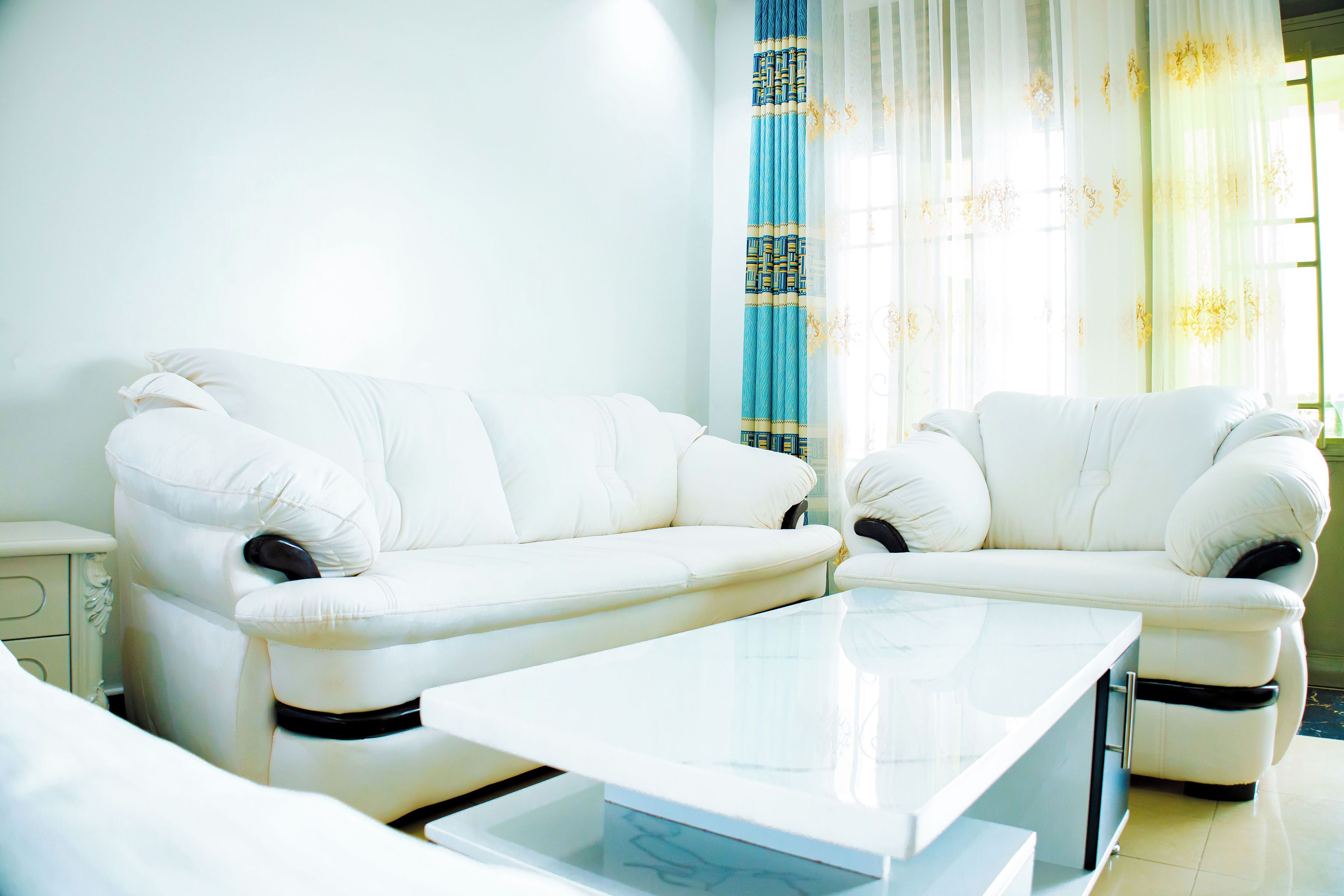 A living room with a white sofa set and a glass coffee table.