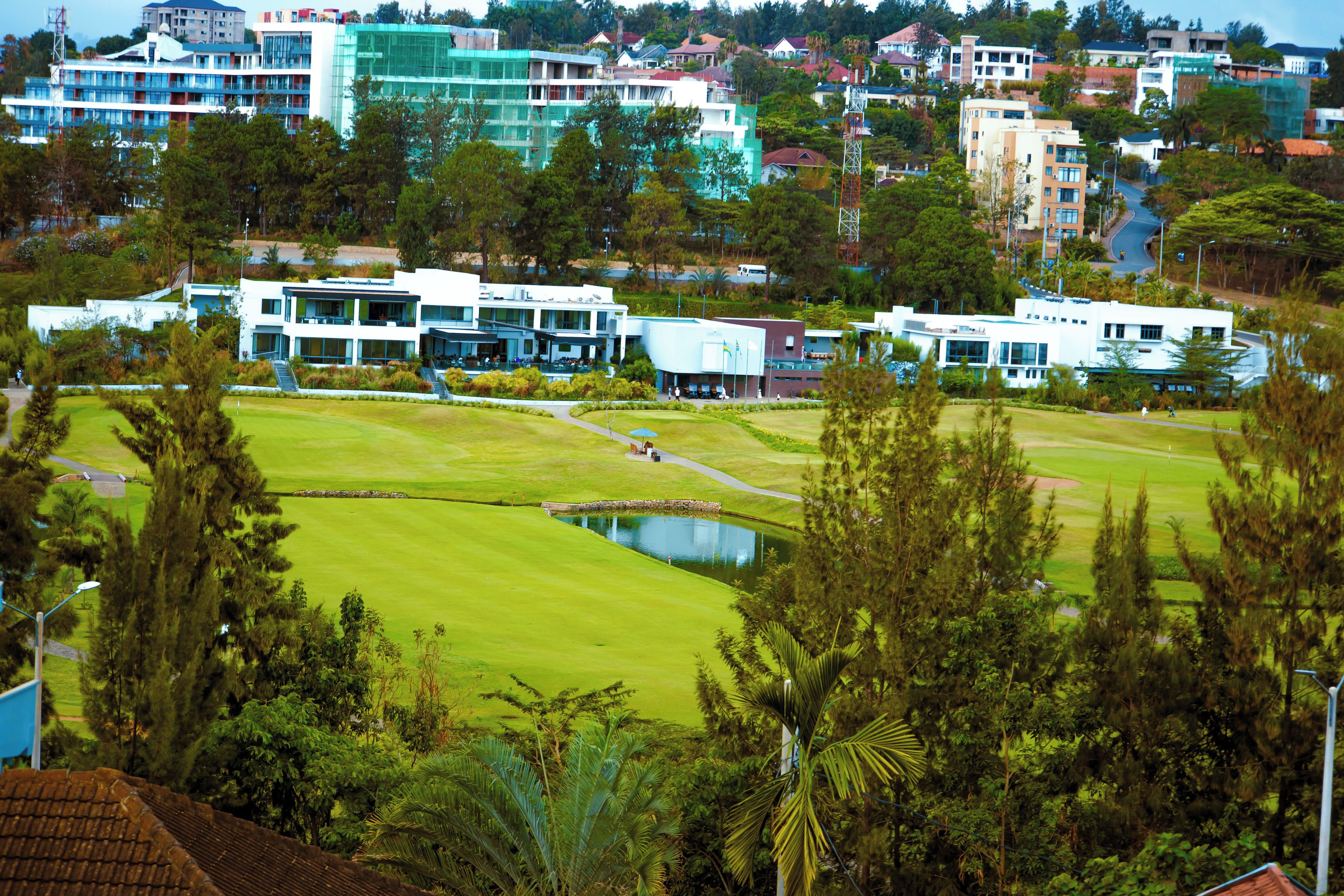 A golf course with a pond, surrounded by modern buildings and trees.