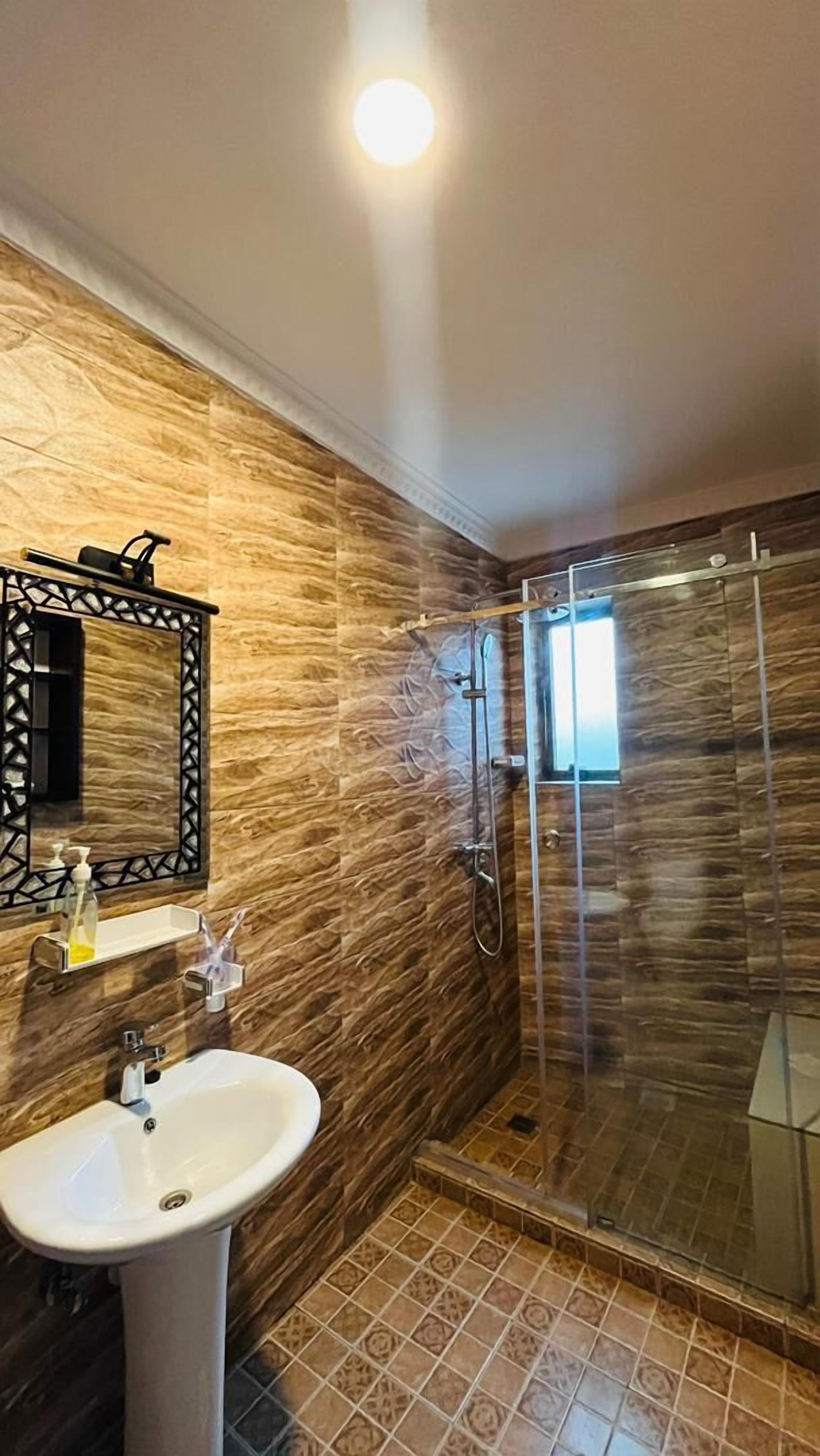 A bathroom with a stone wall, a white sink, a mirror with a black frame, and a glass-enclosed shower.