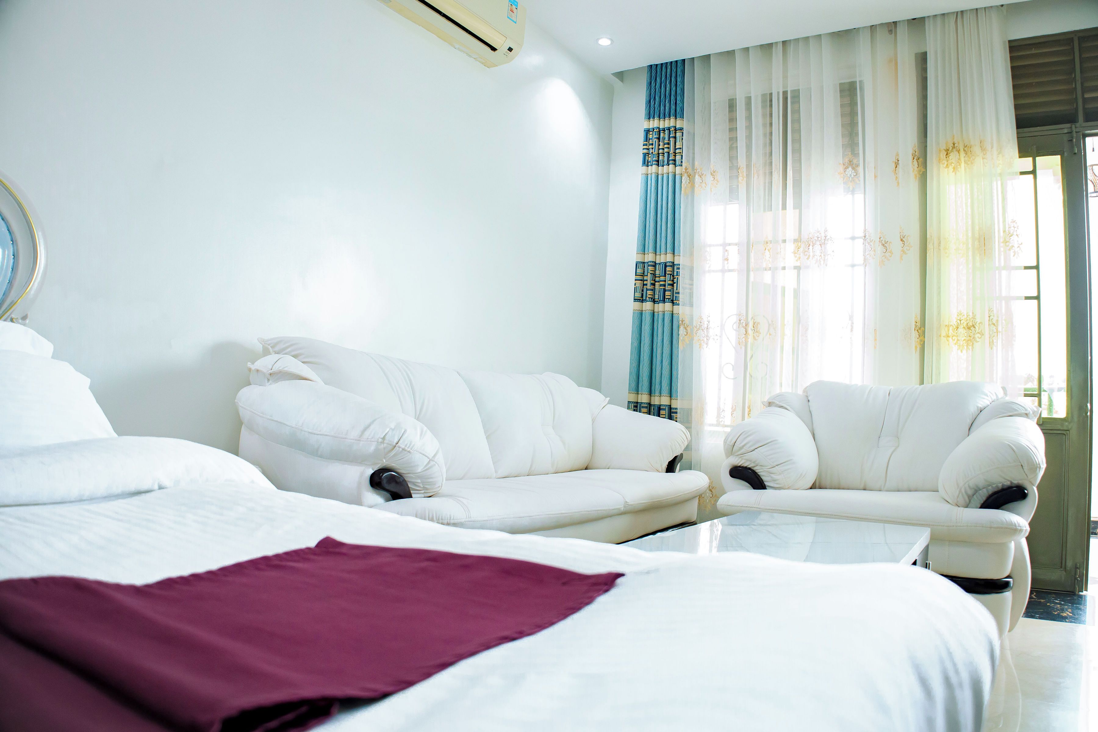 A hotel room with a bed, two white sofas, a coffee table, and a large window with curtains.