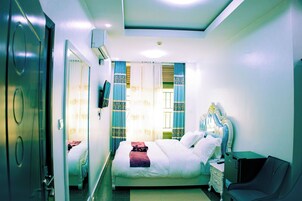 Una habitación de hotel con cama, mesita de noche, silla y ventana con cortinas.