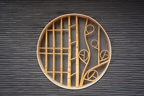 Una reja circular de bambú con un diseño de cuadrícula y adornos en espiral sobre una pared texturizada.