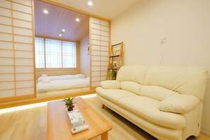 A room with a sofa, a wooden table, and a sliding shoji screen door leading to a bed. - Pleasant Dream Japanese Residence (Osaka)