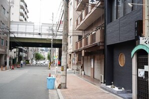 A street with buildings, a blue trash bin, and a closed shop with a sign. - Pleasant Dream Japanese Residence (Osaka)
