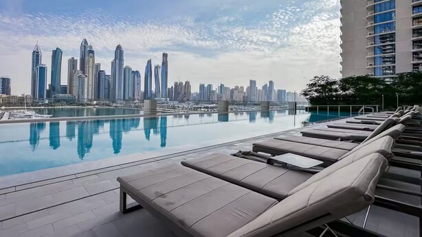 A rooftop pool with lounge chairs, a city skyline view, and a high-rise building in the background. - Marina Vista Residences - Dubai Marina (Dubai)