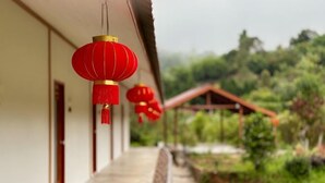 A corridor with red lanterns hanging, a wooden structure in the background, and a garden area.