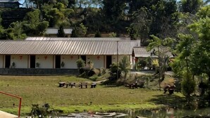 A traditional building with a tiled roof, surrounded by a grassy area with a pond and picnic tables.
