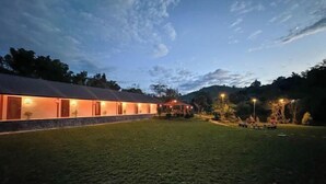 A building with a long, covered outdoor area, possibly a restaurant or cafe, with outdoor seating and a grassy lawn.