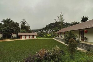 A hotel with multiple buildings, a grassy courtyard, and trees in the background. - Baan Daeng Resort (Mae Hong Son)