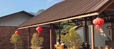A covered outdoor seating area with tables and chairs, stone walls, and red lanterns.