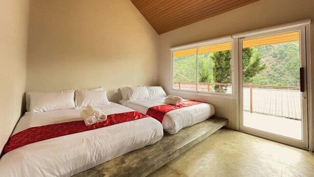 A bedroom with two beds, a wooden ceiling, and a view of greenery outside.