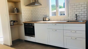 Una cocina moderna con armarios blancos, una campana extractora de acero inoxidable, un horno empotrado y una ventana sobre el fregadero.