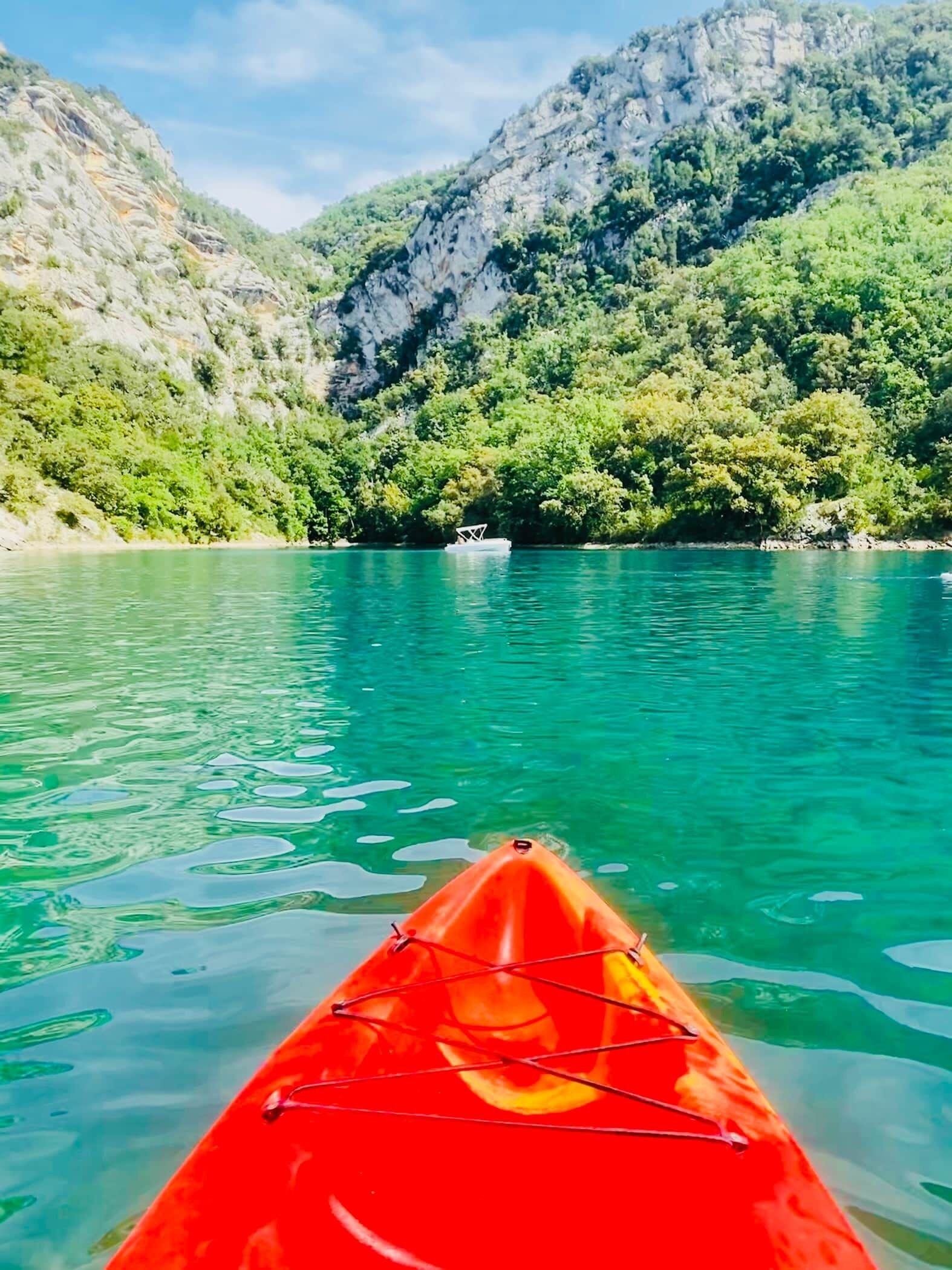 A red kayak on clear turquoise water with a mountainous backdrop.