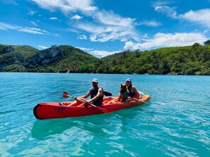 Un kayak rouge sur une eau turquoise et calme, avec une chaîne de montagnes en arrière-plan.