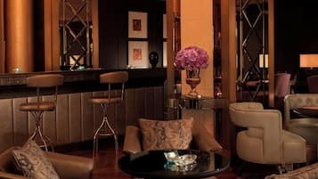 A bar area with high stools, a round table, and a bar counter. There are cushioned chairs and a vase with flowers.