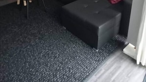 Ein gemütlicher Wohnbereich mit einer schwarzen Couch, einem kleinen Beistelltisch und einem dunkel teppichbelagten Boden.