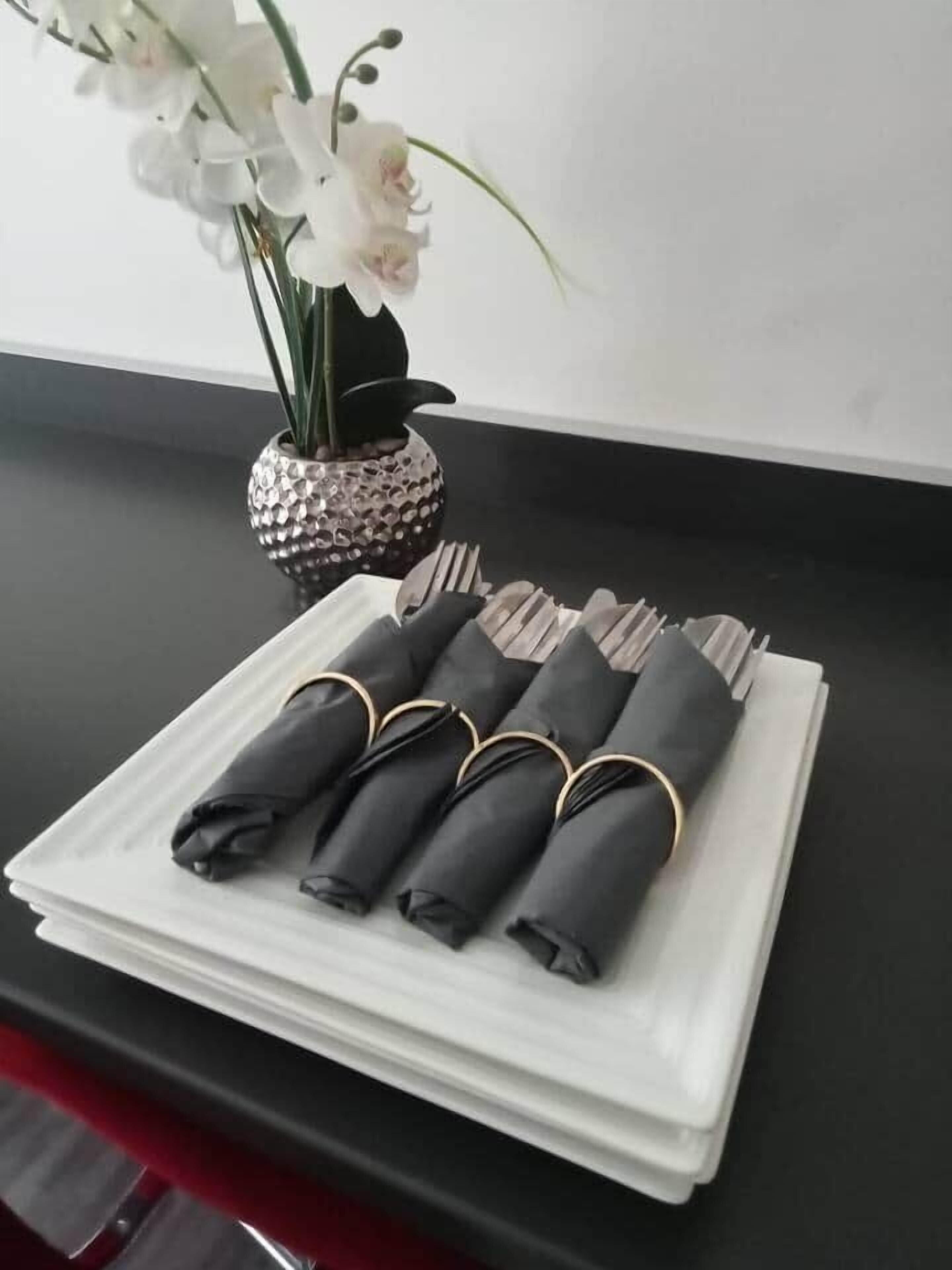 A neatly folded set of black napkins with gold rings on a white napkin holder on a black table.
