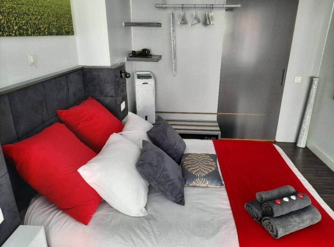 Ein modernes Schlafzimmer mit grauem Kopfteil, einer roten und weißen Tagesdecke und einem roten und weißen Streifen Teppich.