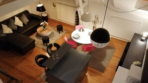 Ein modernes Wohnzimmer mit einer dunkelgrauen Couch, einem runden Couchtisch und einem Essbereich mit einem weißen Tisch und rosafarbenen Stühlen.