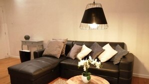 Ein modernes Wohnzimmer mit einem Ecksofa, einem runden Couchtisch mit Blumenvase und einer Pendelleuchte.