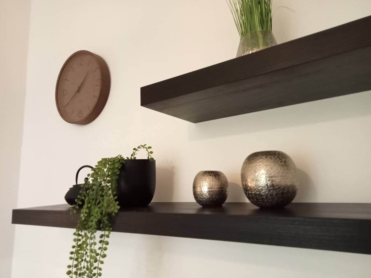 Un reloj de pared, dos estantes oscuros con adornos y una planta en maceta.