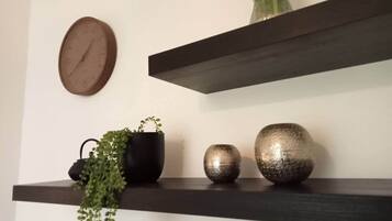 Un reloj de pared, dos estantes oscuros con adornos y una planta en maceta.