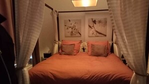 Un lit avec une couvre-lit rouge et deux oreillers, une table de chevet et un mur orné d’œuvres d’art abstraites.