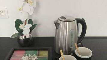 Una mesa negra con un hervidor eléctrico plateado, dos tazas negras con cucharas de madera, un expositor de té enmarcado y un florero con orquídeas blancas.
