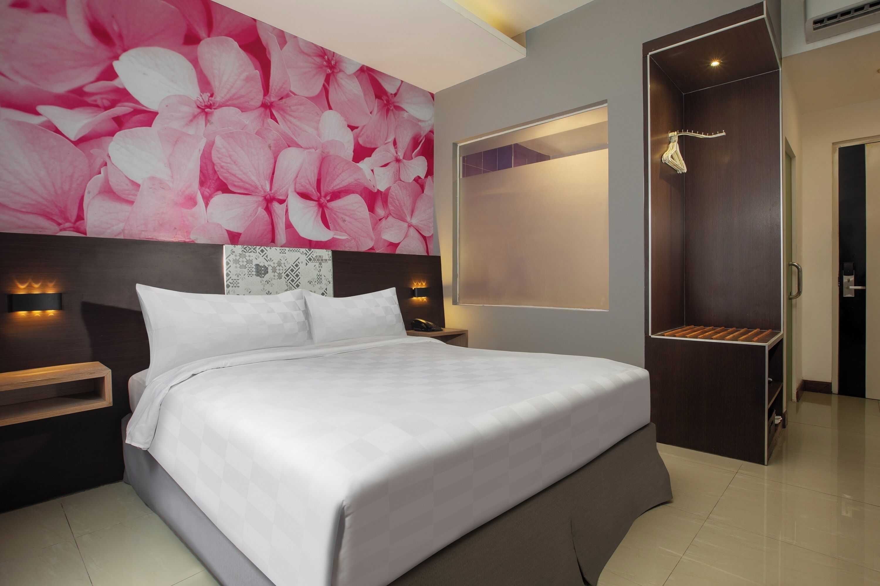A modern hotel room with a large bed, a nightstand, a wall-mounted light, and a wardrobe with a mirror.