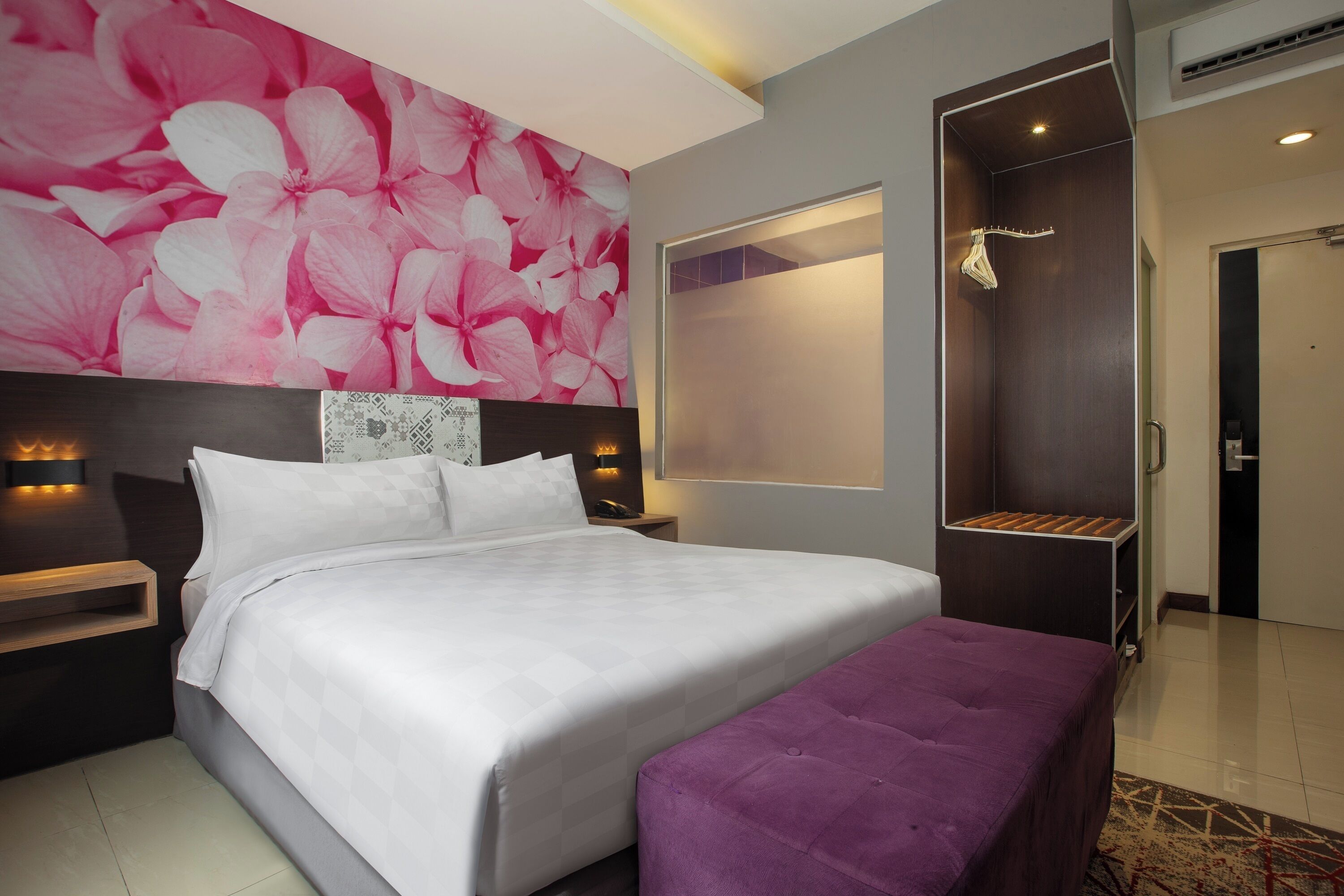 A modern hotel room with a large bed, a shower area, and a vibrant floral wall.