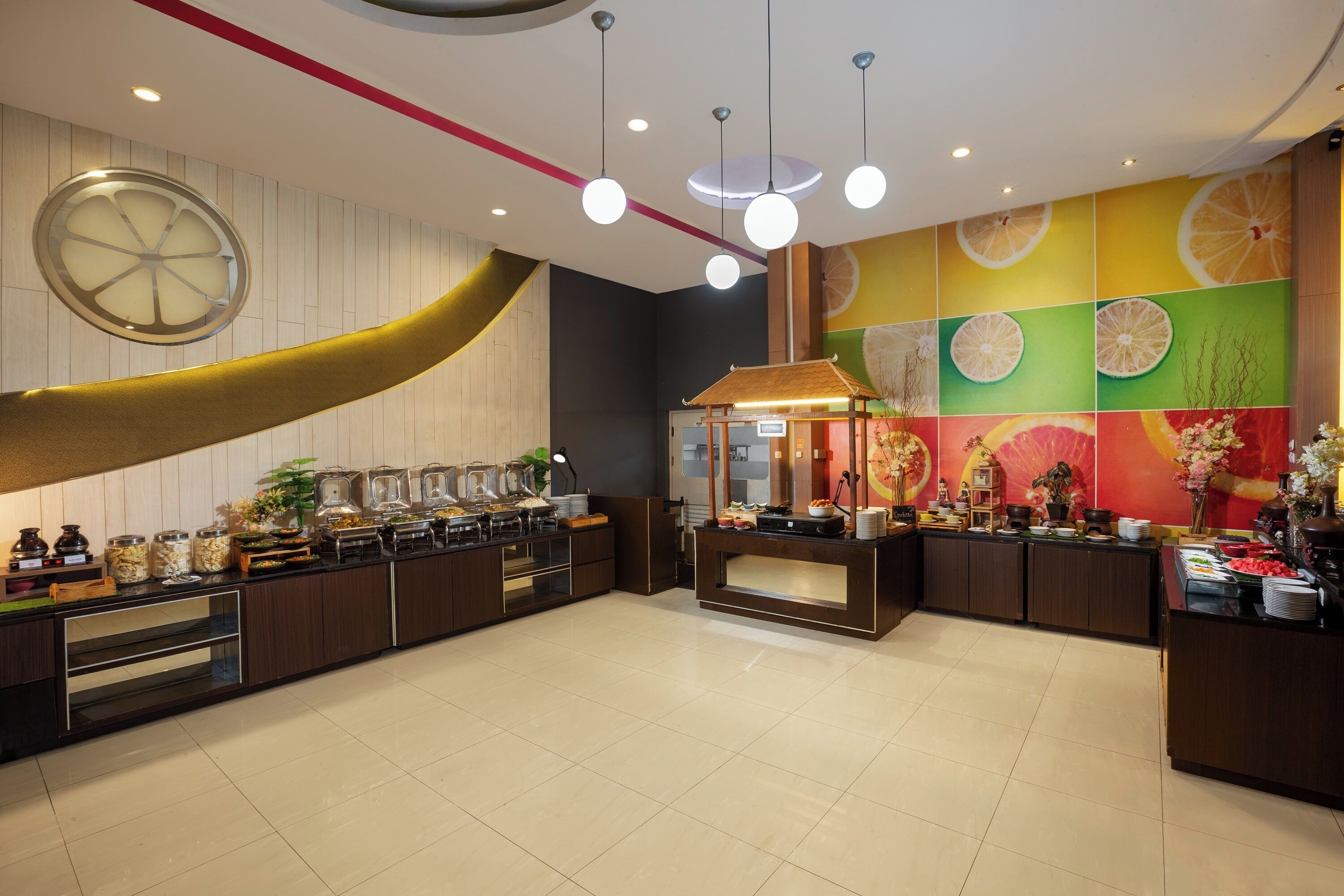 A modern hotel lobby with a buffet area, a large decorative wheel, and a vibrant fruit-themed wall.