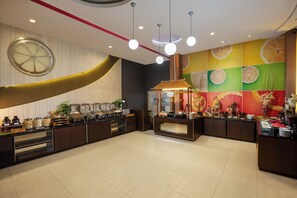 A modern hotel lobby with a buffet area, a large decorative wheel, and a vibrant fruit-themed wall. - Avery Hotel Yogyakarta Kusumanegara (Yogyakarta)