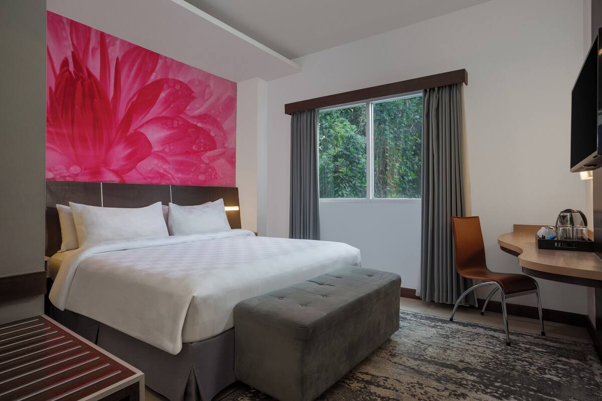 Ein Hotelzimmer mit einem großen Bett, einem Schreibtisch, einem Stuhl und einem Fenster mit Vorhängen.