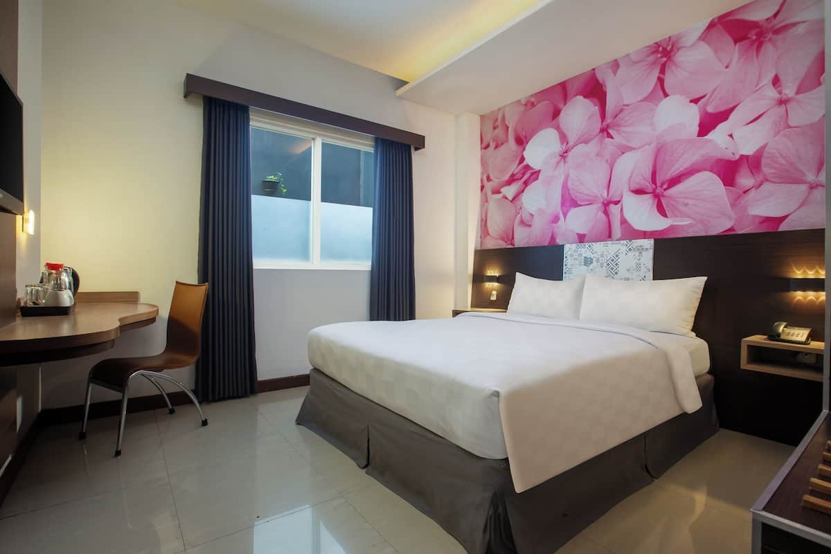 Ein Hotelzimmer mit Bett, Schreibtisch, Stuhl, einem Fenster mit Vorhängen und einer Wand mit Blumenmuster.