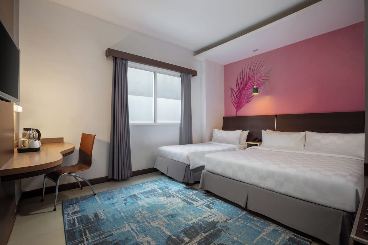 Ein Hotelzimmer mit zwei Betten, einem Schreibtisch, einem Stuhl und einem großen Fenster mit Vorhängen.