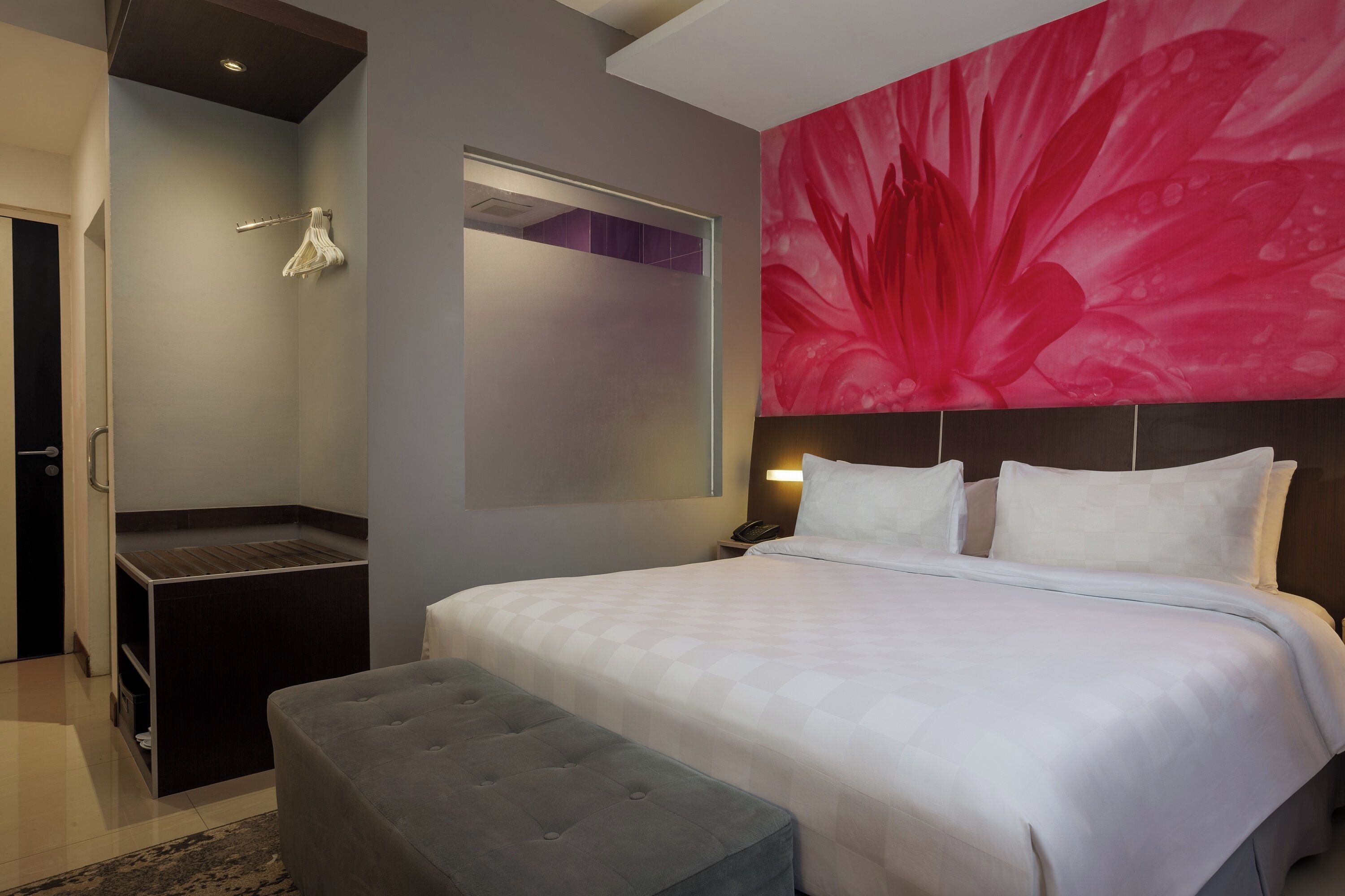Ein modernes Hotelzimmer mit einem großen Bett, einer grauen Bank, einer Duschkabine und einem lebhaften Blumenbild an der Wand.