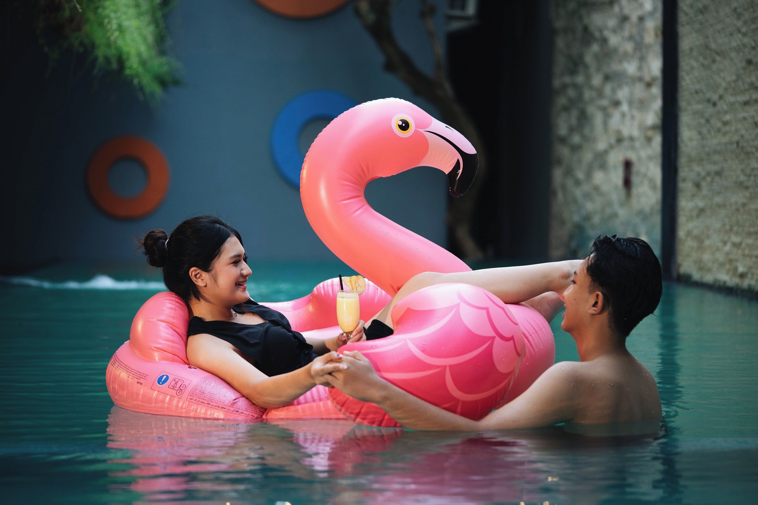Un couple dans une piscine, avec un grand flotteur en forme de flamant rose.
