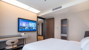 Et moderne hotelværelse med en seng, et skrivebord og et ophængt fjernsyn, der viser en hotelapp.