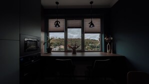 A dark room with a window overlooking a cityscape, a table with chairs, and a potted plant. - Renovated 1BR • City View • Workspace (Chișinău)