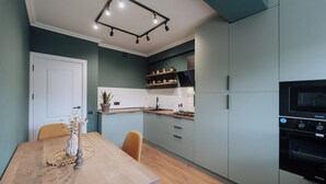 A modern kitchen with light green cabinets, a wooden dining table, and a built-in oven. - Renovated 1BR • City View • Workspace (Chișinău)