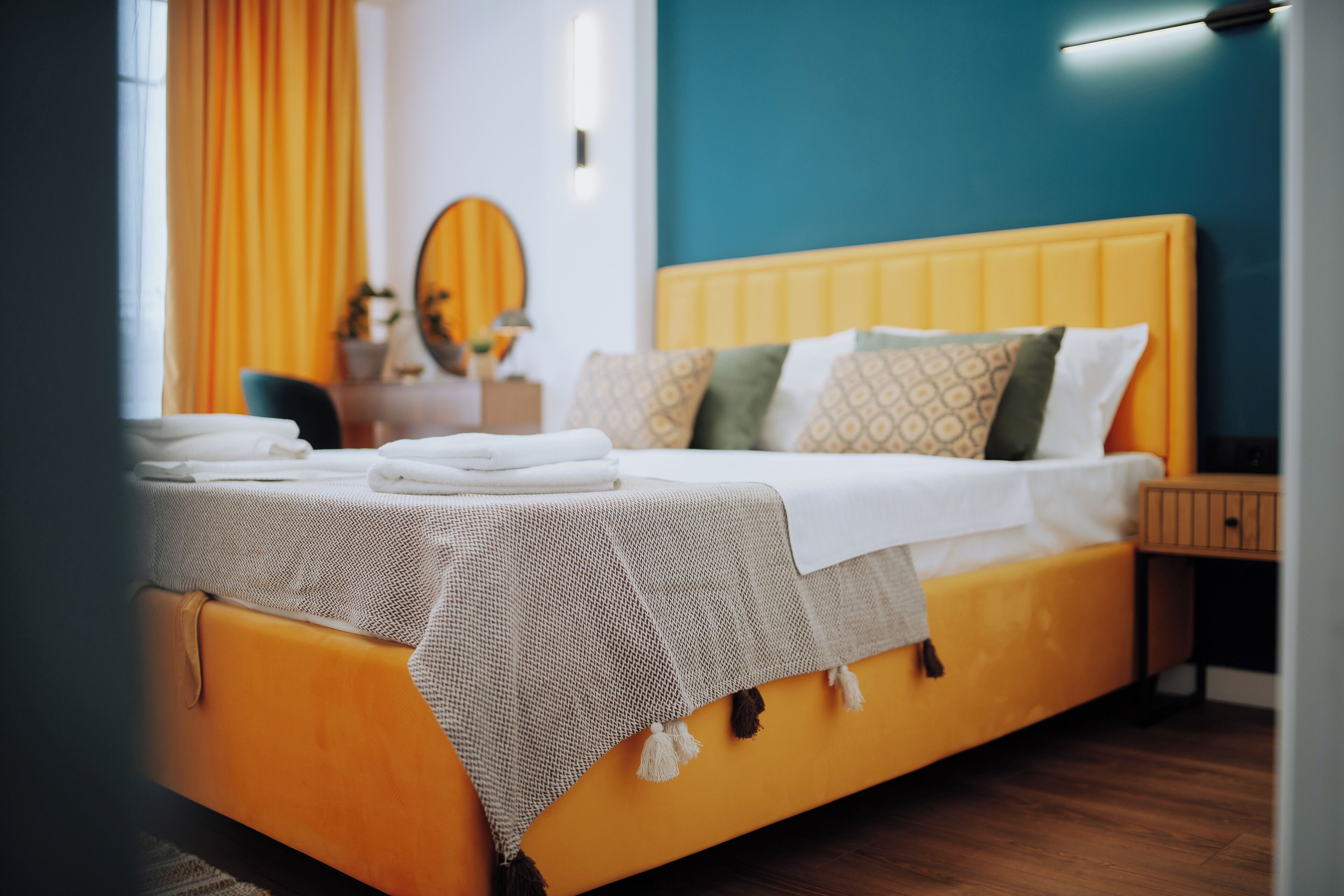 Una cama bien hecha con cabecera amarilla, sábanas blancas y una colcha estampada.